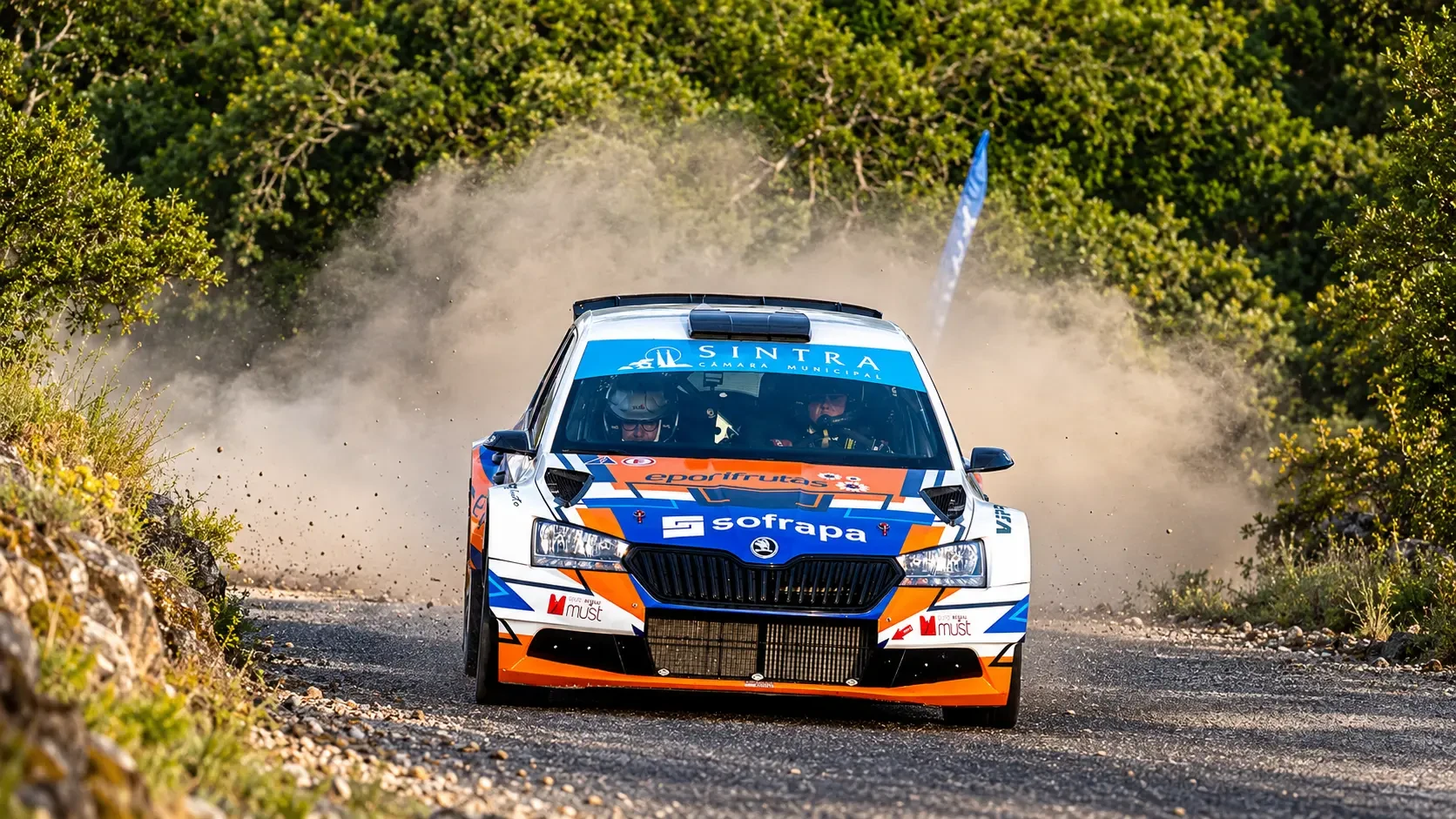 Škoda de rali azul, branco e laranja numa estrada de terra